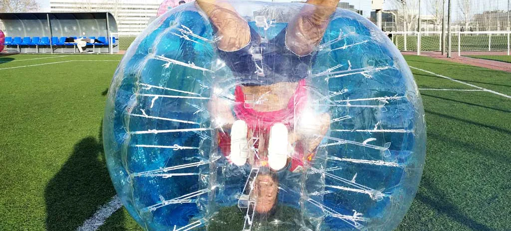 Jugador dentro de una burbuja de PVC rodando sobre el campo durante una partida de fútbol burbuja en Madrid.